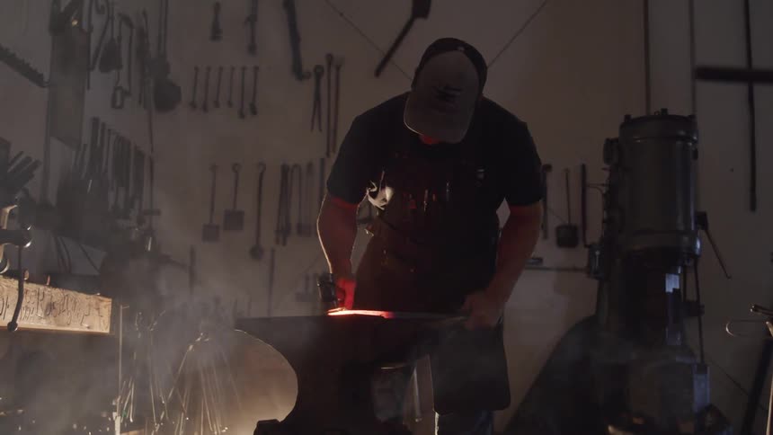 Blacksmith hammering metal over anvil with hammer at workshop