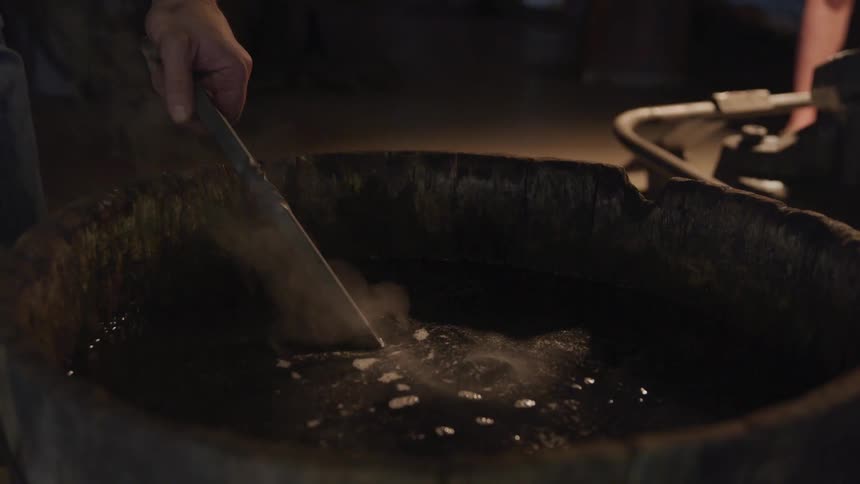 Man pulls a tool out of a large pot of boiling liquid