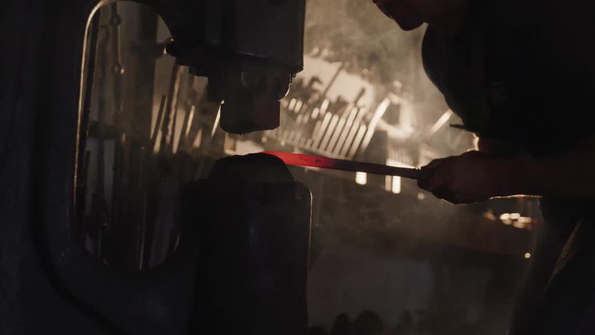 Man shaping hot metal with the use of a large machine indoors