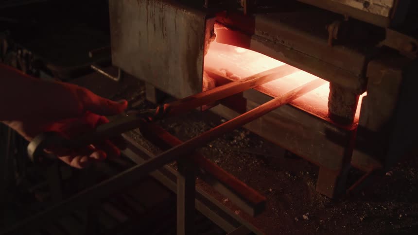 A person pulls a piece of metal from a red hot industrial oven