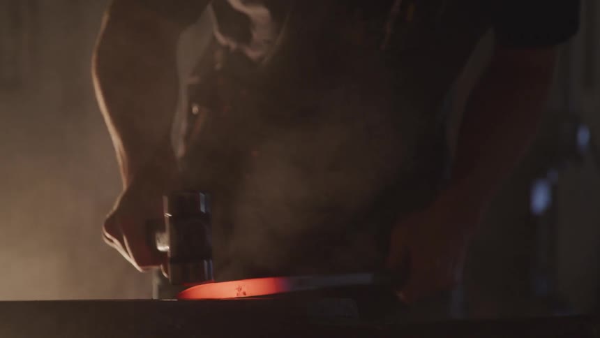 A blacksmith hammering the red hot end of a piece of metal