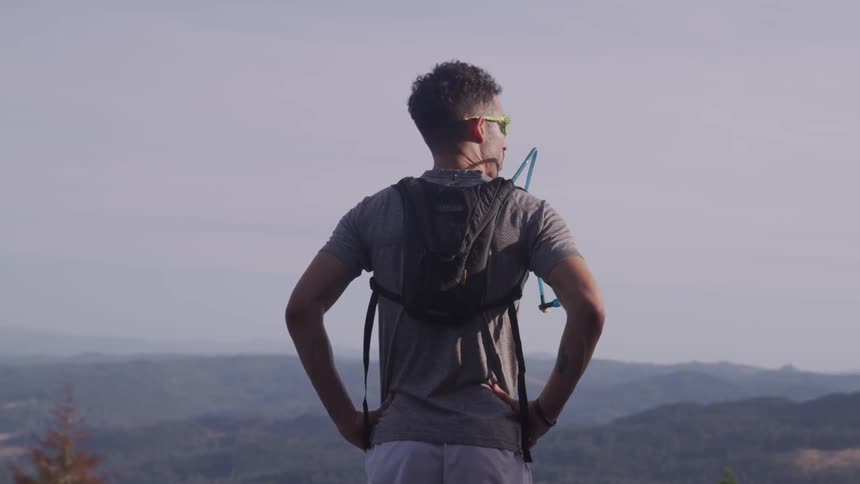 A man stands high above a valley at looks across the horizon