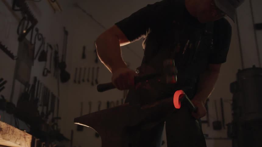 A man is using a small sledgehammer on a hot piece of metal