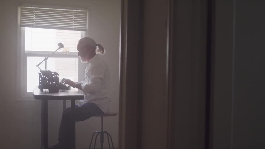 Man sitting at a desk typing on a typewriter