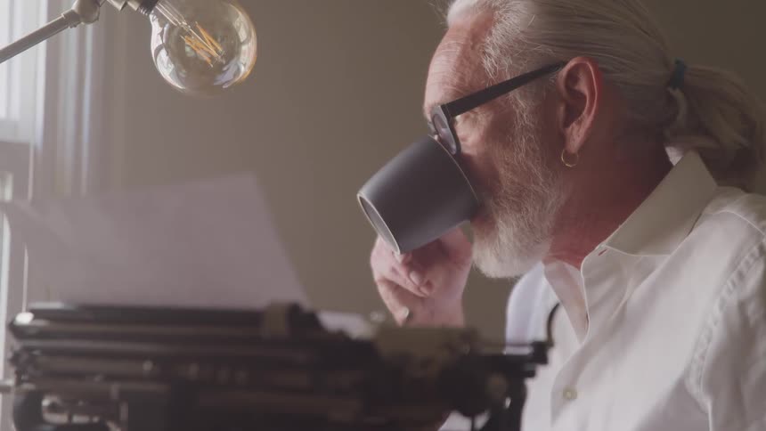 A man drinks from a coffee cup looking out a window