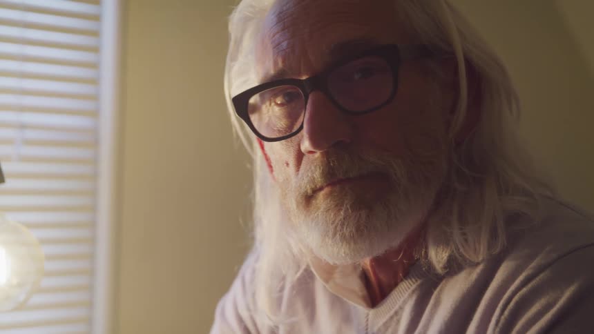 Senior long hair bearded man turns to the camera in a room