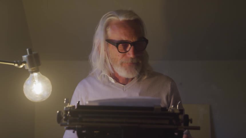 A man lights a cigarette sitting in front of a vintage typewriter