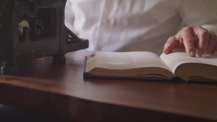 Man reads the book and types on typewriter in a room