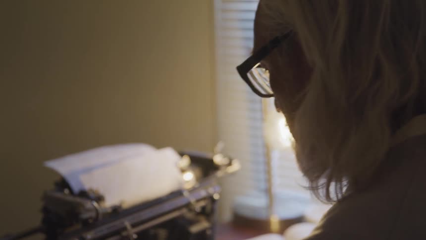 A man wipes his eyes while sitting at a typewriter