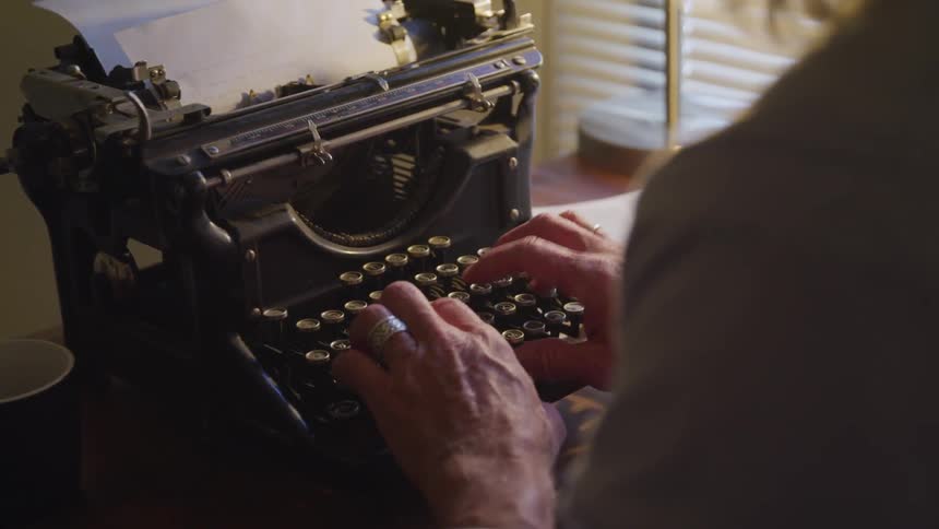 A man sits and types on an old typewriter
