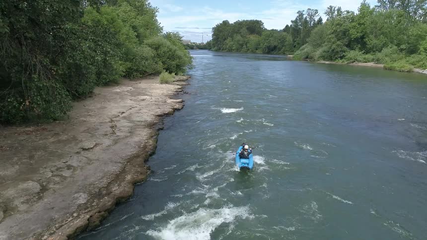 Person wearing a white helmet steering a kayak with a paddle down the rapid water near the bank of the river