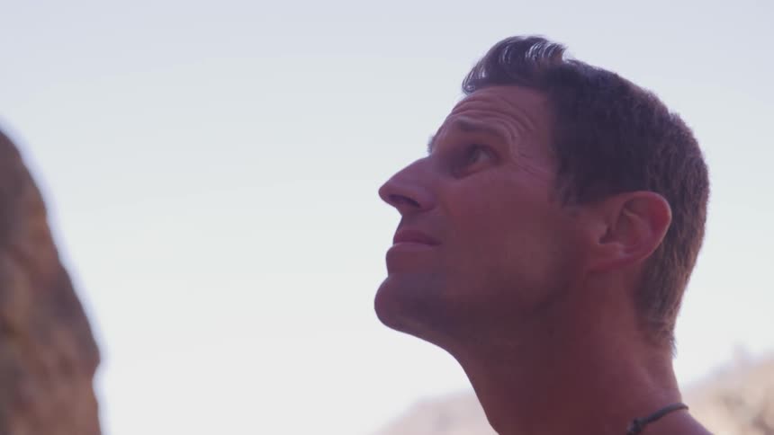 A man stands at the base of a mountain and looks up