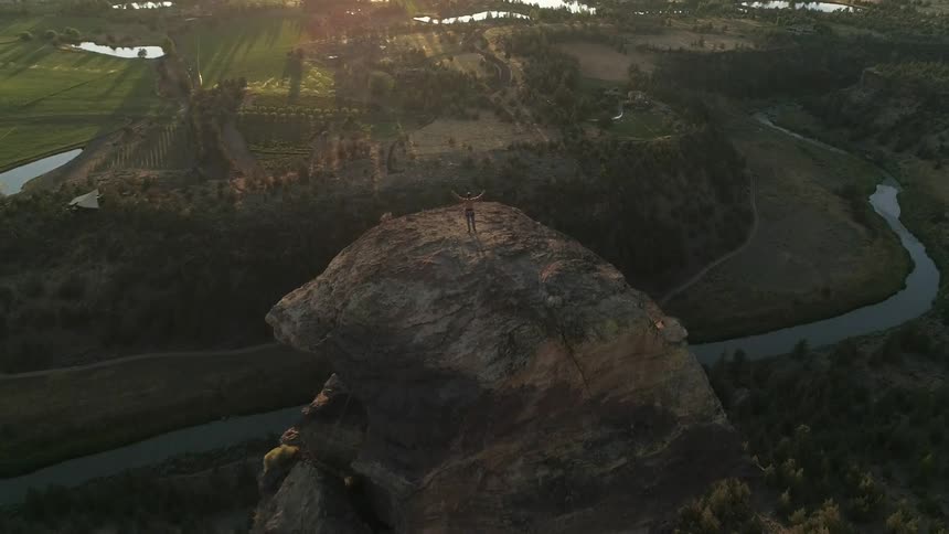 A hiker stands on top of a summit and raises his arms