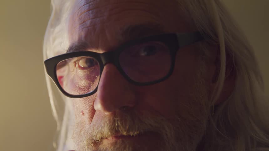 Senior long hair and bearded man looks at the camera in a room