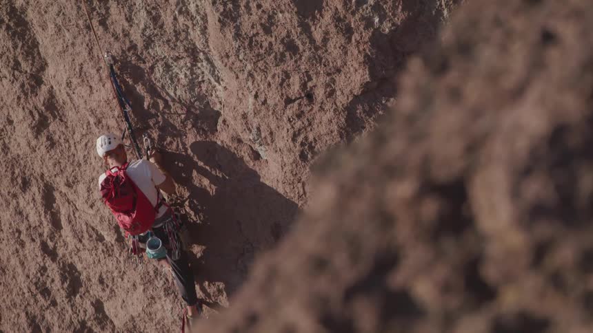 A man in a helmet attaches a rope to a hook while climbing a rock