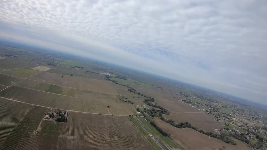 A skydivers hands in straps of an open parachute as they soar over the landscape