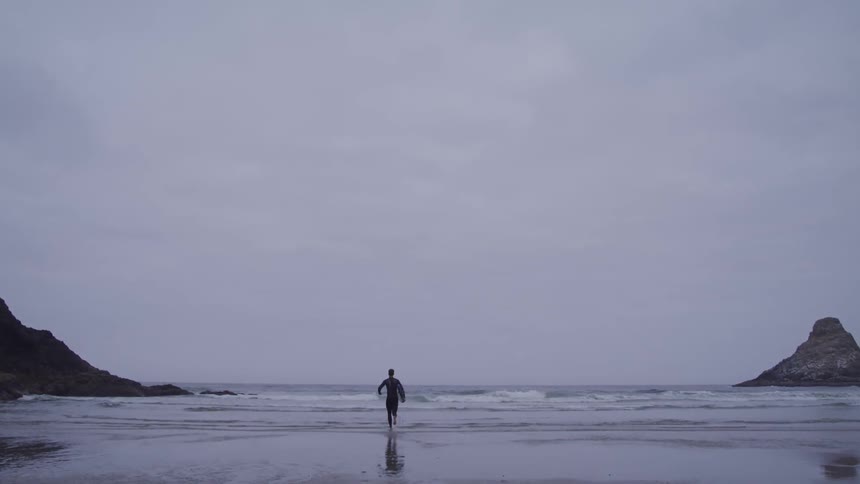A man runs toward the ocean with a board