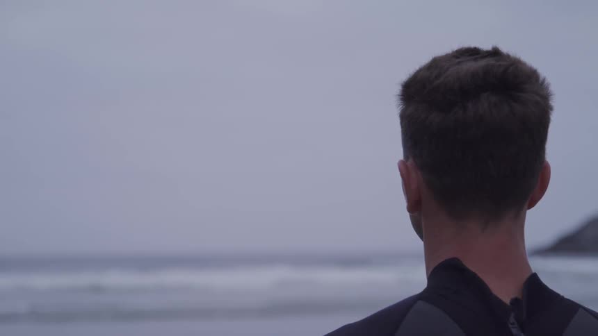 Man stands on the beach next to the sea and on a cloudy day