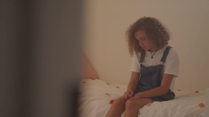 A child is sitting on a bed and looking sad