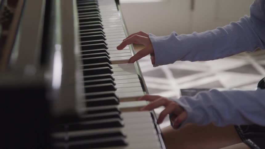 A young female sits at a piano and reaches out with her fingers to press some of the keys