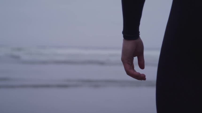 A person wearing a wet suit looks towards the ocean as they stand on a beach