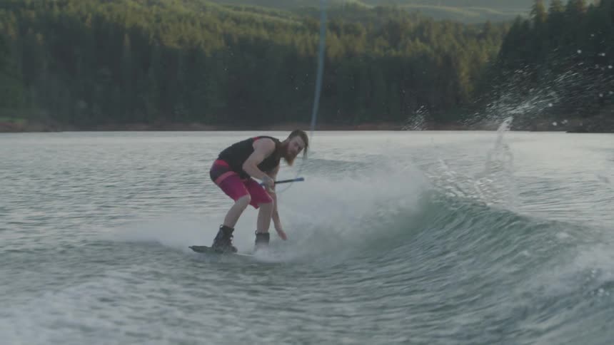 A man using a wave to do a flip while wakeboarding in a lake