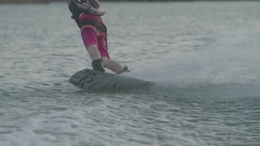 A person cuts across the surface of the water while holding a towline as they are wakeboarding