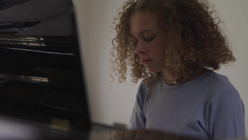 Curly red hair girl plays the piano in a room
