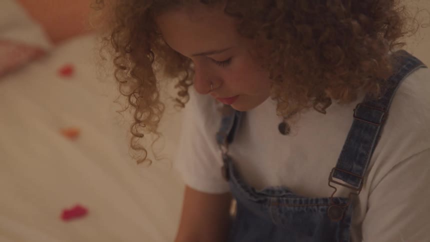 Curly red hair girl sit on the bedmorosely contemplating in a room