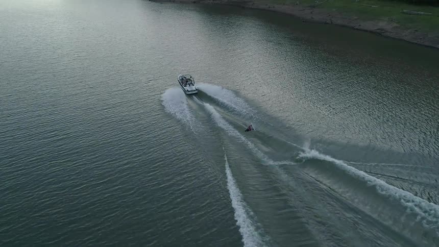 A boat is moving through a lake and someone is doing water sports