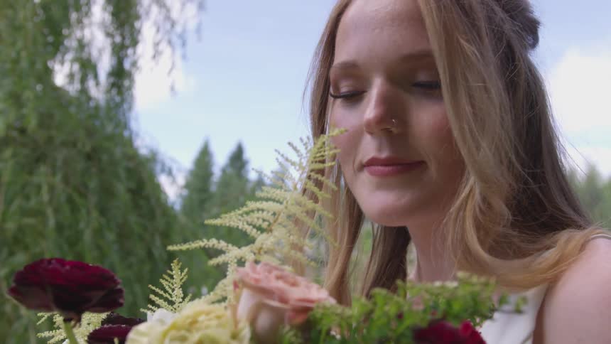 Bride holds and smells a bouquet of flowers in the public park