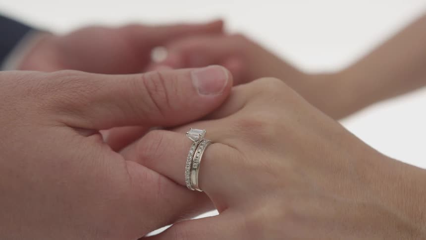 A woman with diamond rings holds hands with a man