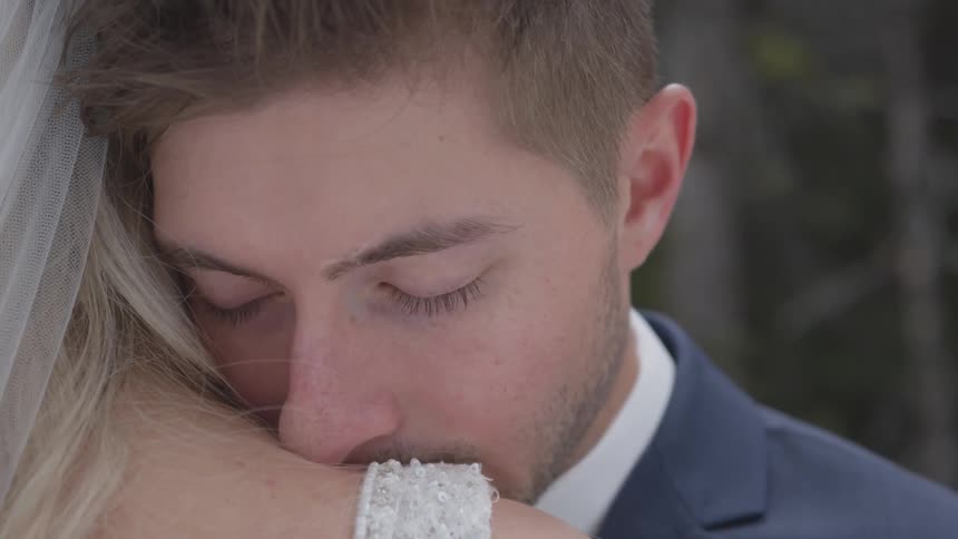 Groom in a suit cuddles bride during the wedding ceremony