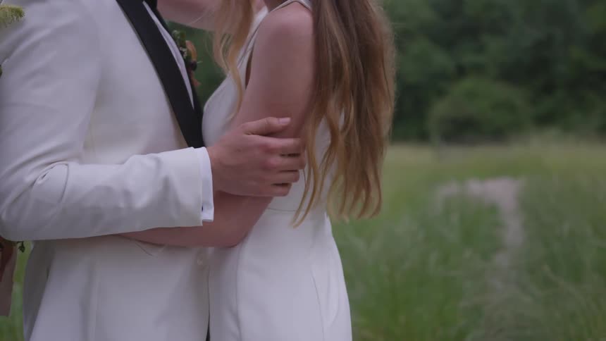 A bride and groom embrace standing in a grass area