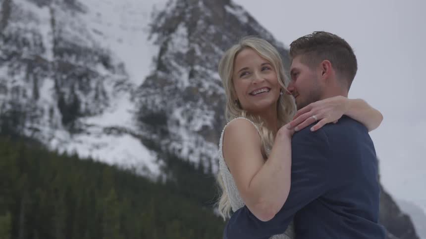 A husband and wife hug each other with a snow covered mountain behind them