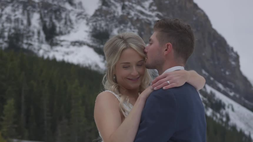 Newlyweds embracing and smiling in front of snow covered mountain