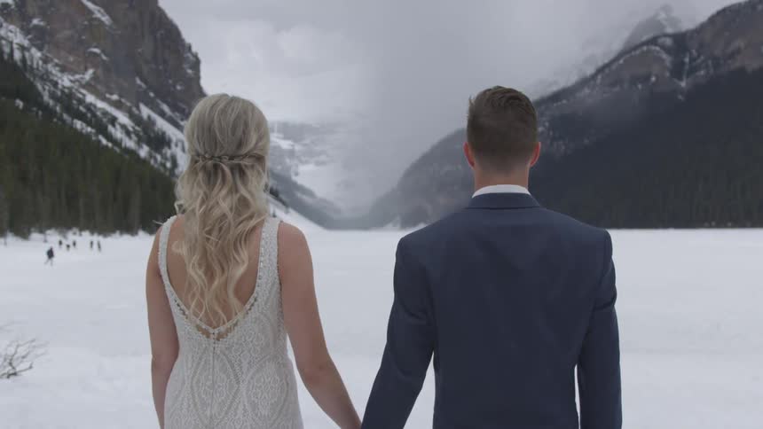A woman in a dress and a man in a suit standing in a snowy mountain valley