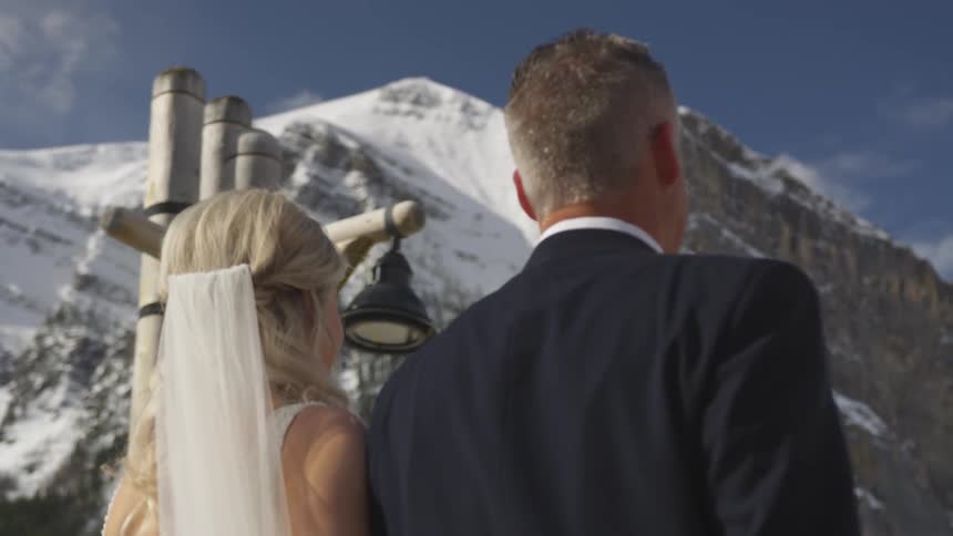 A bride and groom walk in the snowy mountain