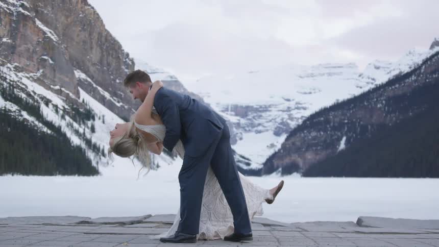 A bride and groom dance by the snow covered mountains