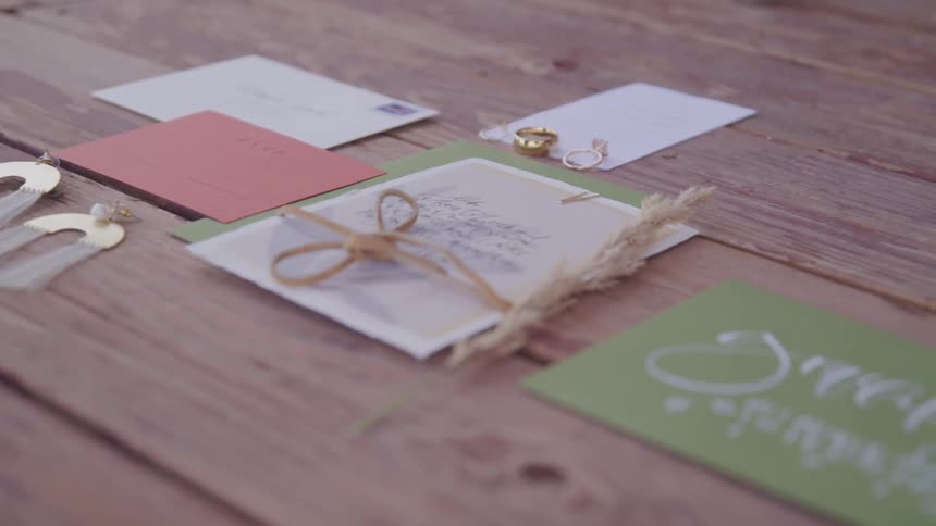 Several letters and postcards are situated around two wedding rings that are sitting atop a wooden table