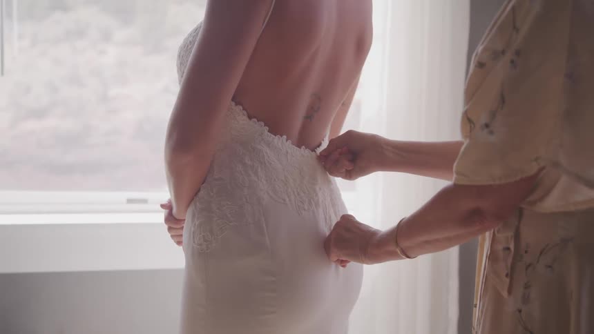 Mother helping her daughter with the back zipper on her wedding dress