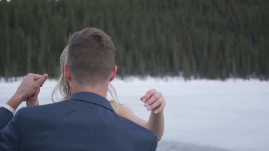 A bride and groom smile while embracing outside in a snowy forest