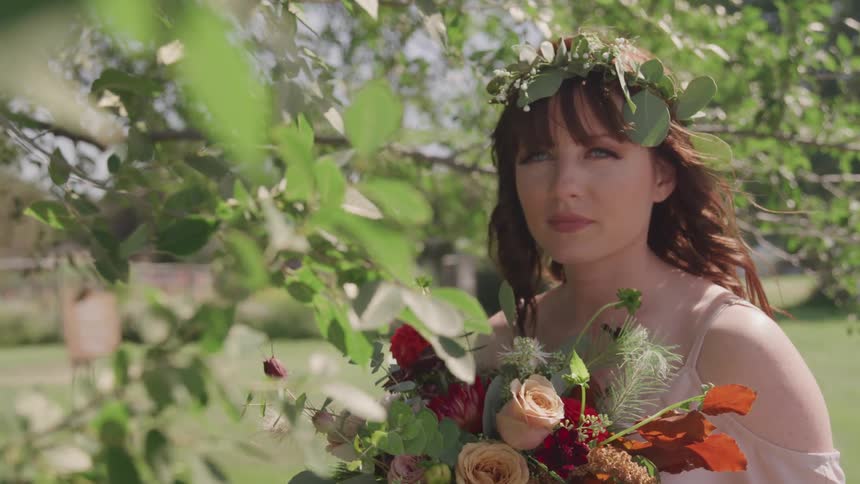 A woman holds a bouquet standing under a tree