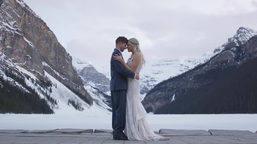 A bride and groom embrace by snow covered mountains
