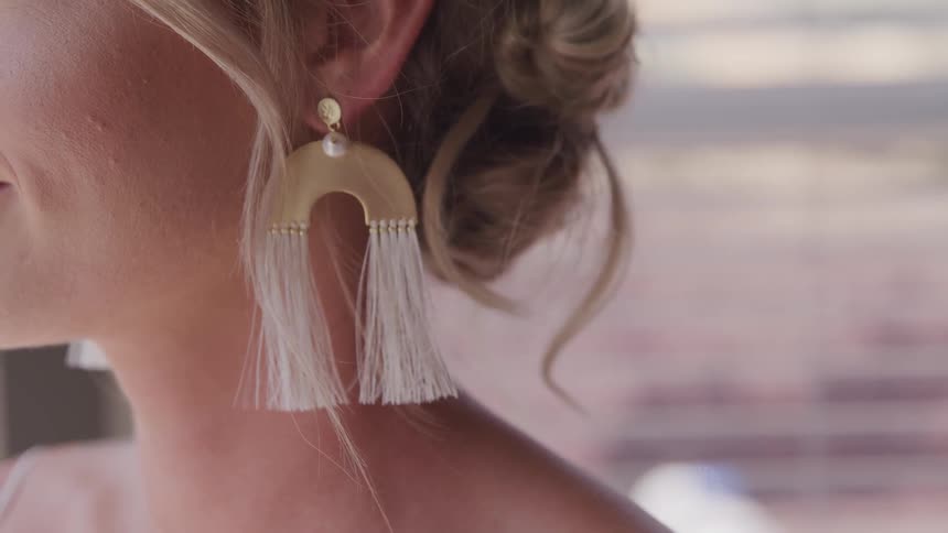 A woman with professional makeup and hair wearing large white fringed earrings
