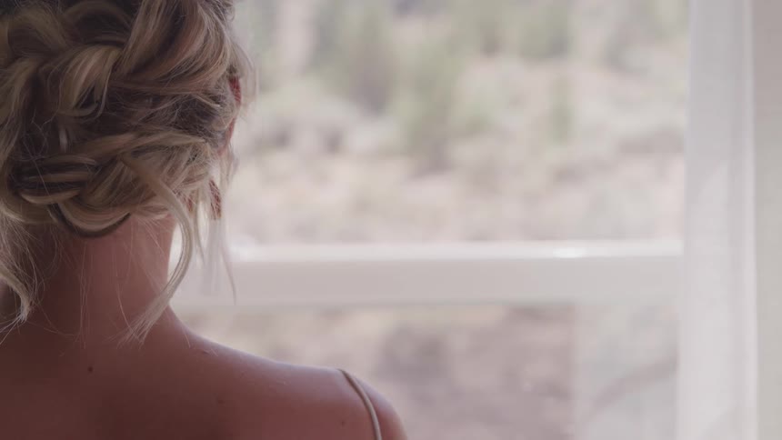 A blonde haired woman looks away from the camera and out a window on a sunny day