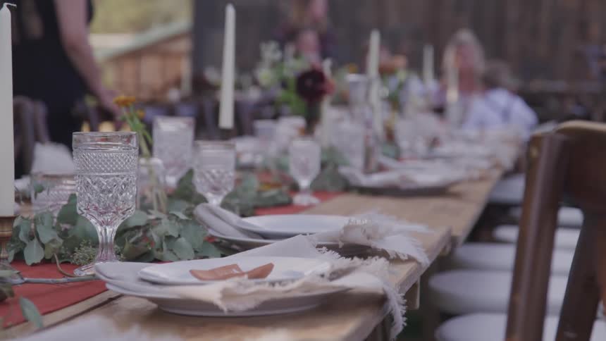 A large table chairs and place settings with a crowd of people in the distance