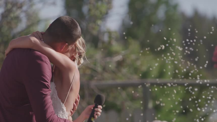 People shower the kissing bride and groom with white confetti on a sunny day
