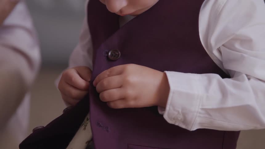 Little boy puts on waistcoat during the day