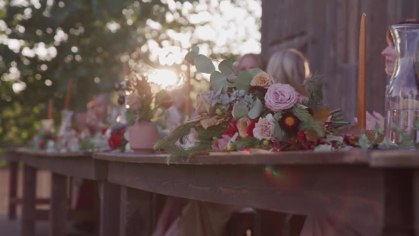 Bridesmaids sitting at wooden table outdoors at sunset near barn